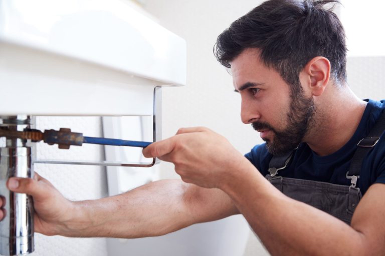 male plumber using wrench to fix leaking sink in h RL9MYZ7